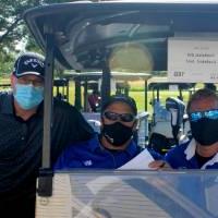 three alumni posing with a golf cart